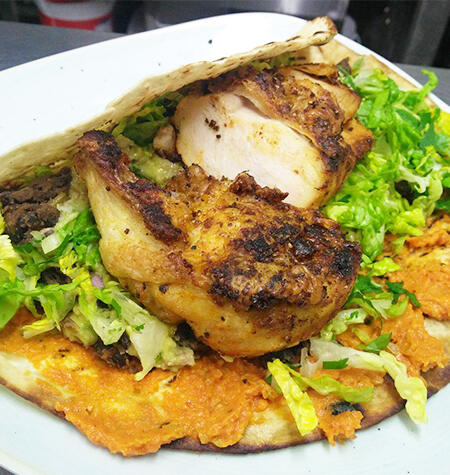 Spiced chicken on a flatbread with leaves on a white plate