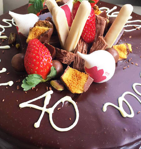 A chocolate celebration cake with honeycomb, strawberries and white chocolate lettering