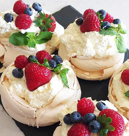 Mini pavlovas topped with cream, berries and mint on a slate board